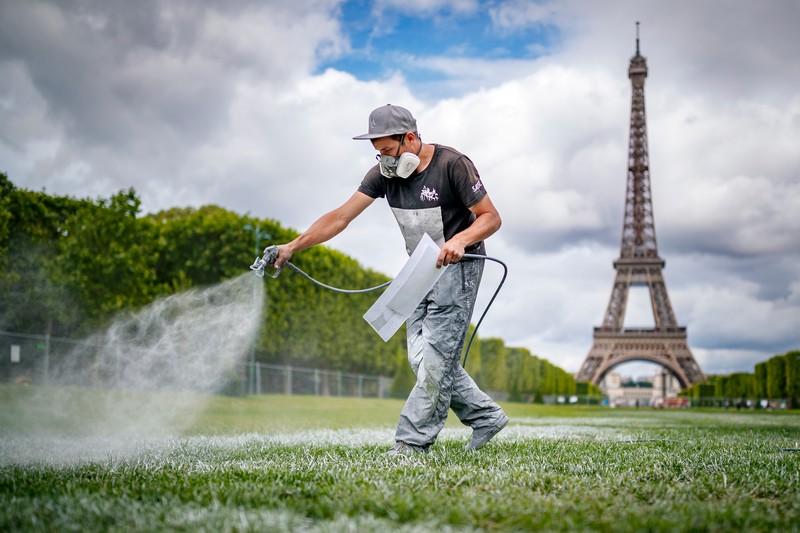 Artist Saype at work, spraying biodegradable paint onto grass during the "Beyond Walls" project at the foot of the Eiffel Tower, Paris, 2019. Photo: MTArt Agency and Saype.