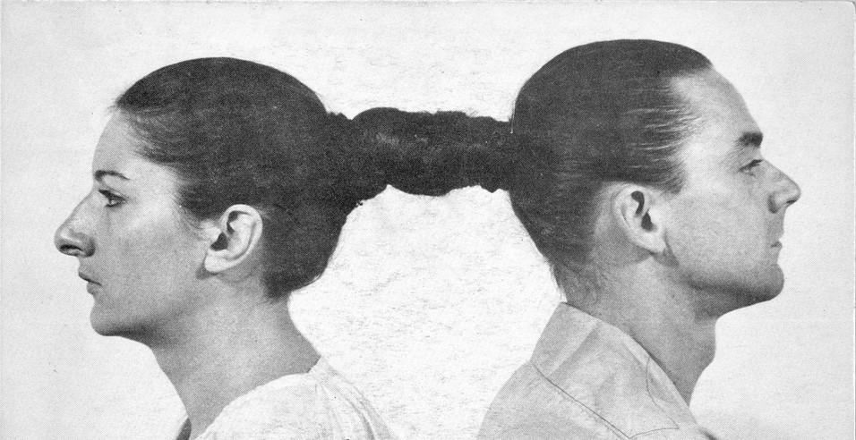 Performance by artist Marina Abramović, in which she sits back-to-back with her partner, their hair intertwined in a single braid (Leipzig, Germany, 1978). Photo: Wikipedia.